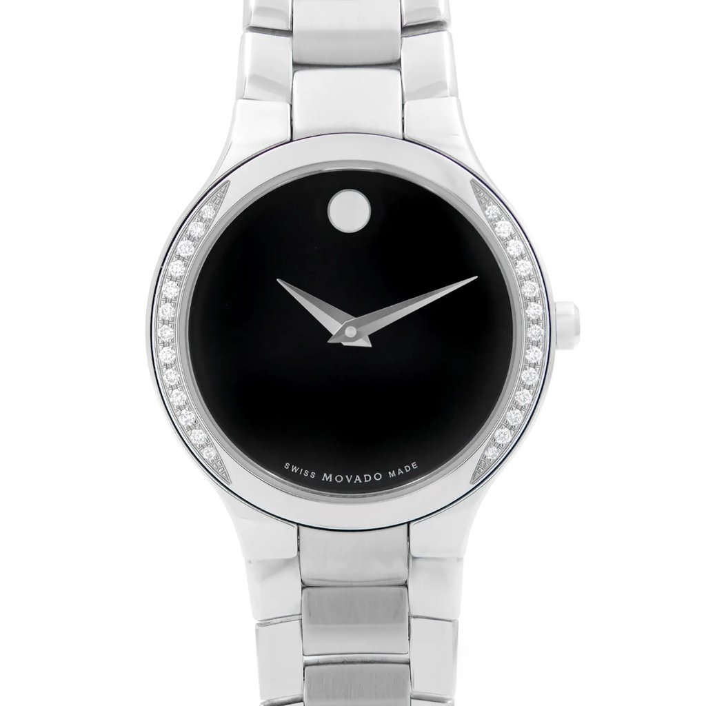 An image of a front close-up view of an unworn Movado women's wristwatch. The watch features a round black dial with a minimalist design, accented by a single dot at the 12 o'clock position and steel-colored hands. Surrounding the dial is a bezel adorned with diamonds, providing a formal appearance. The case and band are made of stainless steel, with the band visible in the foreground, leading into the watch face. The angle of the shot is head-on, focusing on the watch face with the band partially visible and tapering off into the distance. With "Swiss Movado Made" is inscribed at the bottom of the dial.