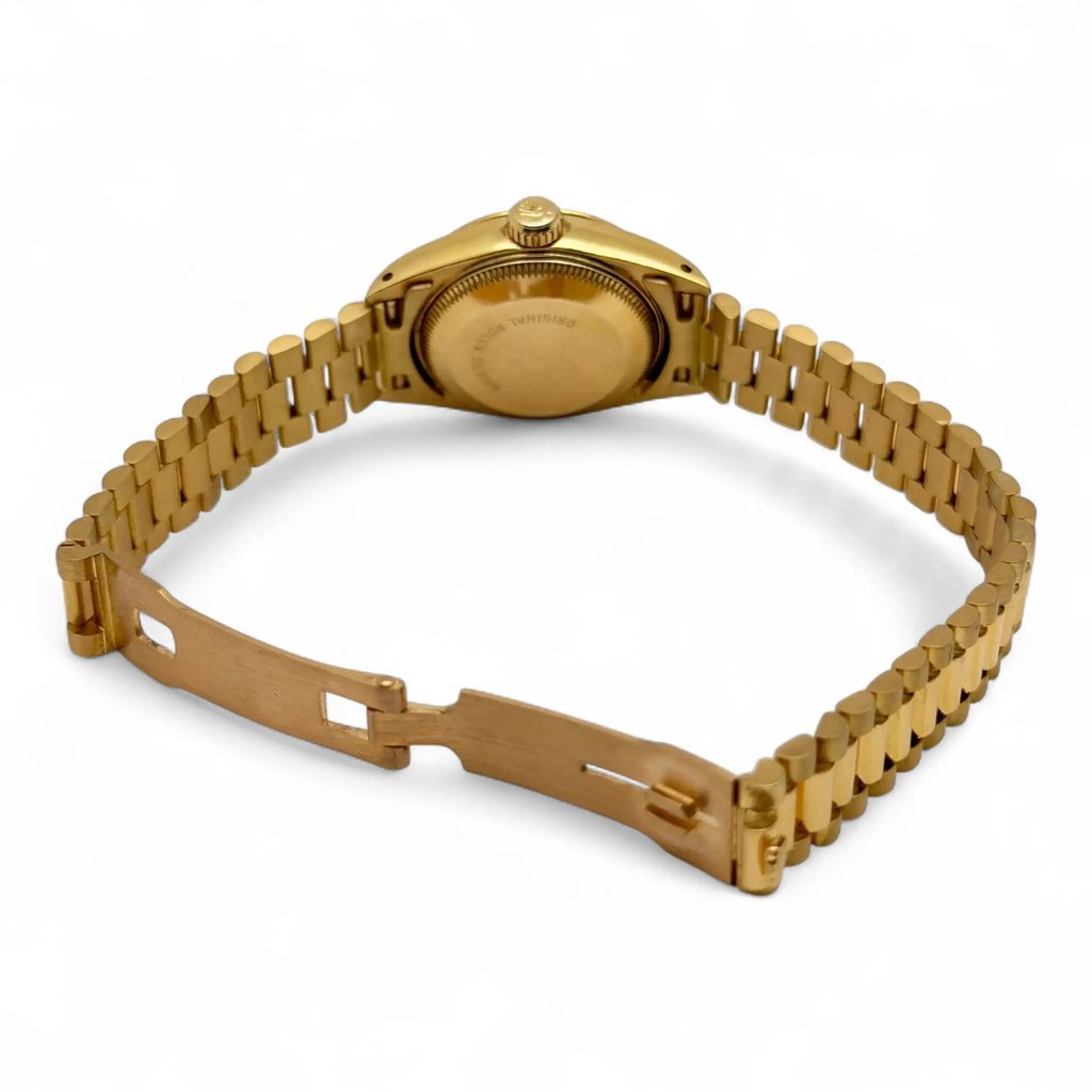An image of a pre-owned women's Rolex wristwatch, featuring a yellow gold bracelet and a date indicator. The watch is positioned at a slight angle from the back, showcasing the closed clasp and case back. The photograph is taken at a close distance, highlighting the details of the gold links and the watch's overall polished appearance.