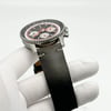 An image of a Breitling men's wristwatch in display model condition, showcased at a side angle with the watch face tilted upwards towards the camera. The watch features a chronograph, date indicator, and luminous hands, along with a small seconds subdial. It is positioned on a white-gloved hand against a white background, allowing clear visibility of the watch details. The black leather band shows discoloration consistent with storage, and the watch is in close-up view, providing a detailed look at the textures and design elements.