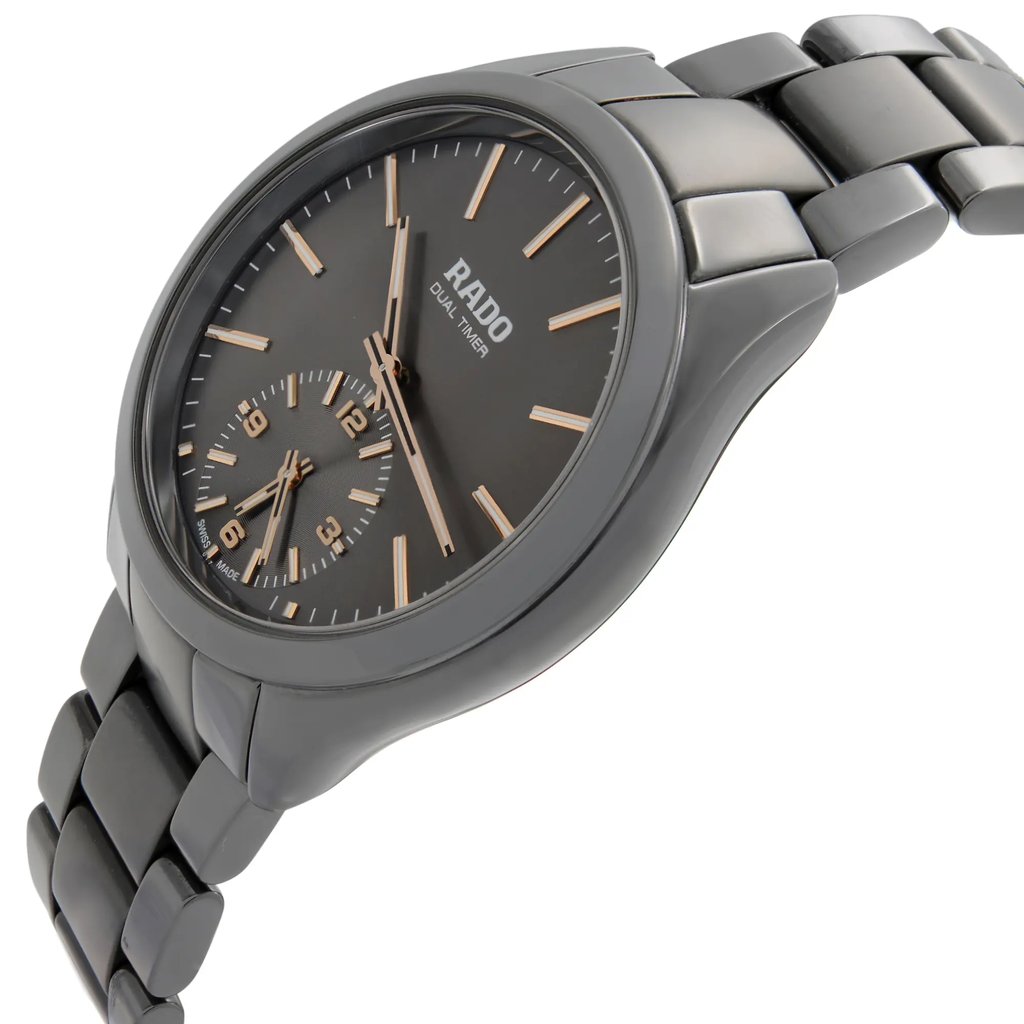 An image of a wristwatch displayed from a side profile view, highlighting the crown on the right side. The watch features a sleek, metallic design with a dual-time display on its dark dial. The bracelet is visible, showcasing its polished links. The photograph captures the watch at a slight angle, emphasizing its stylish contours and craftsmanship, typical of a display model.