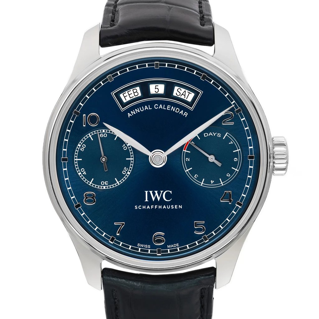 An image of a pre-owned wristwatch taken from a front close-up angle, showcasing the watch face in detail. The watch features a blue dial with an annual calendar display, including the day, date, and month. It has two subdials and silver-tone hands with numerals around the edge. The timepiece is paired with a black leather strap.