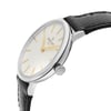 An image of a wristwatch shown from a side profile view, focusing on the unworn condition. The watch's crown is prominently displayed, positioned to the right. The watch face features a white textured dial with gold hour markers and hands. The case is metallic, paired with a black textured leather strap, photographed at a close angle to highlight the details.