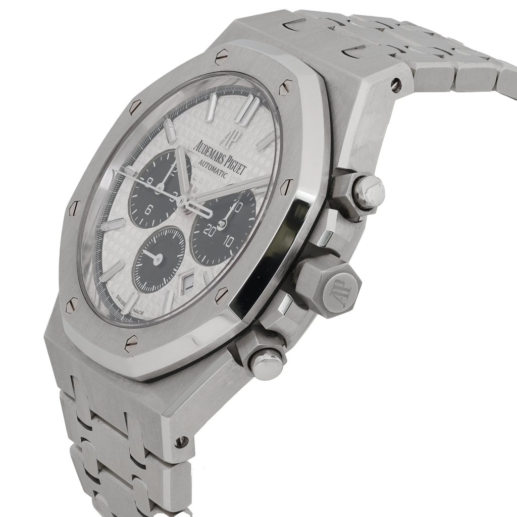 An image of a pre-owned men's Audemars Piguet wristwatch taken at a slight angle, showcasing the watch face and part of the bracelet. The watch features luminous hands and a sophisticated design with a stainless steel case. The close-up shot highlights the intricate details of the dial and the brand's logo, with the side buttons and crown visible on the right.