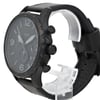 An image of a Fossil wristwatch positioned at a slight angle from the front, showcasing the watch face and side buttons. The watch features a black dial with large numerals and three sub-dials. The black leather strap is visible, with the watch resting on a transparent stand. The photo is taken at a close distance to highlight the details, such as the textured bezel and prominent crown. The watch condition is marked as new with defects.
