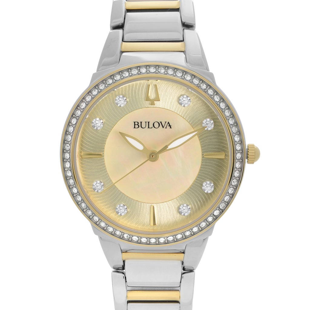 An image of a front close-up shot of a women's Bulova wristwatch, displayed as a model. The watch features a round champagne-colored, mother of pearl dial pattern with gold-tone luminous hands and non-numeric hour marks indicated by small diamonds. A gold-tone bezel set with diamonds surrounds the dial. The band is made of stainless steel with gold-tone center links. The watch is shown from a direct front angle with the face centered and taking up most of the frame, providing a clear view of its elegant details.