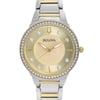 An image of a front close-up shot of a women's Bulova wristwatch, displayed as a model. The watch features a round champagne-colored, mother of pearl dial pattern with gold-tone luminous hands and non-numeric hour marks indicated by small diamonds. A gold-tone bezel set with diamonds surrounds the dial. The band is made of stainless steel with gold-tone center links. The watch is shown from a direct front angle with the face centered and taking up most of the frame, providing a clear view of its elegant details.