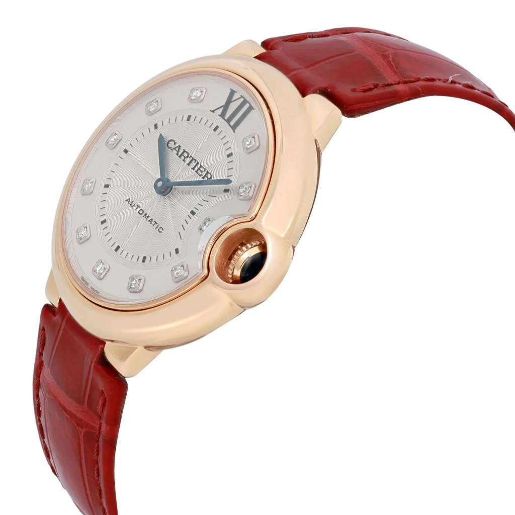 An image of a pre-owned Cartier women's wristwatch positioned at a slight angle, showcasing its elegant design. The watch features a rose gold case and a unique asymmetric shape, with a silver dial and diamond hour markers. The watch is equipped with blue hands and a prominent crown adorned with a blue cabochon. Attached to a red leather strap, the watch is captured from a close-up perspective, highlighting its luxurious details.