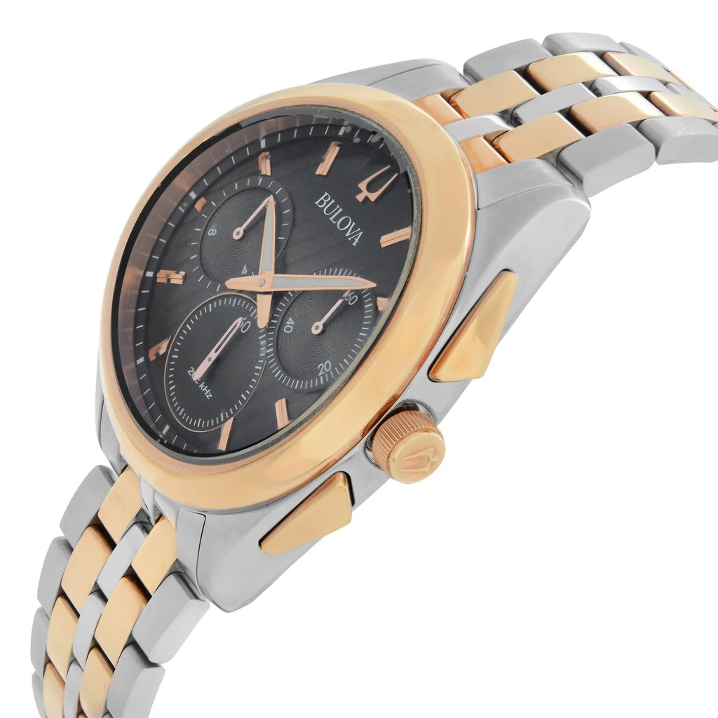 An image of a pre-owned Bulova men's wristwatch in a side profile view with the crown visible. It features a round black dial with gold-toned luminous hands and chronograph sub-dials, encased in stainless steel with a gold bezel. The watch is attached to a two-tone stainless steel bracelet. The angle of the photo provides a clear view of the watch's side, showing the texture and design details on the crown and the curvature of the case and bracelet. The watch is positioned at a close distance, making it appear large in the frame for detailed inspection.
