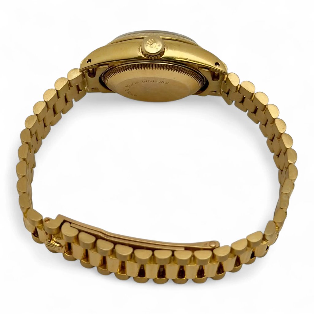 An image of a pre-owned women's Rolex wristwatch, viewed from the back at a slight angle. The focus is on the yellow gold bracelet and the back of the watch case, displaying the brand's logo on the crown. The watch features a date indicator, although it is not visible from this angle. The watch is positioned centrally and photographed from a medium distance against a plain white background.