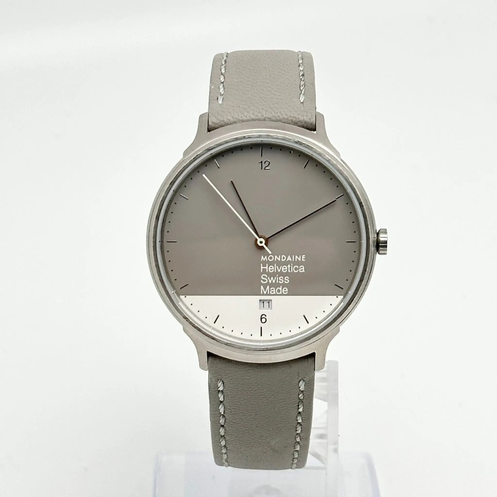 An image of a Wristwatch by Mondaine. This Pre Owned item is designed for Unisex Adult, featuring a Casual style. It has a Quartz movement and an Analog display with a Gray-White dial color. The indices include 12-Hour Dial,Arabic Numerals,Stick Indexes. The band is made of Leather and the case is made of Stainless Steel. The watch has a Round shape with a case size of 38 mm and a case thickness of 7 mm.