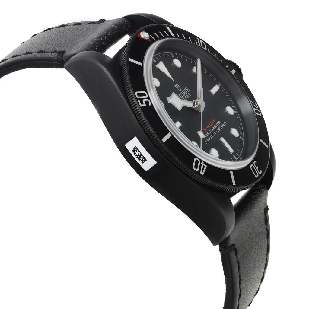 An image of a wristwatch in a side profile view, opposite the crown. The watch displays a black dial with luminous markers and a black bezel, set within a robust case. The angle highlights the watch's thickness and contour, showing the leather strap extending from the case. The watch is a display model, photographed from a close distance, emphasizing the texture and detailing of the materials.