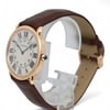 An image of a pre-owned Cartier unisex wristwatch positioned at a slight angle on a clear stand. The watch features a round face with Roman numerals and a dark brown leather strap. The photograph is taken from a close distance, highlighting the sleek design and gold casing.