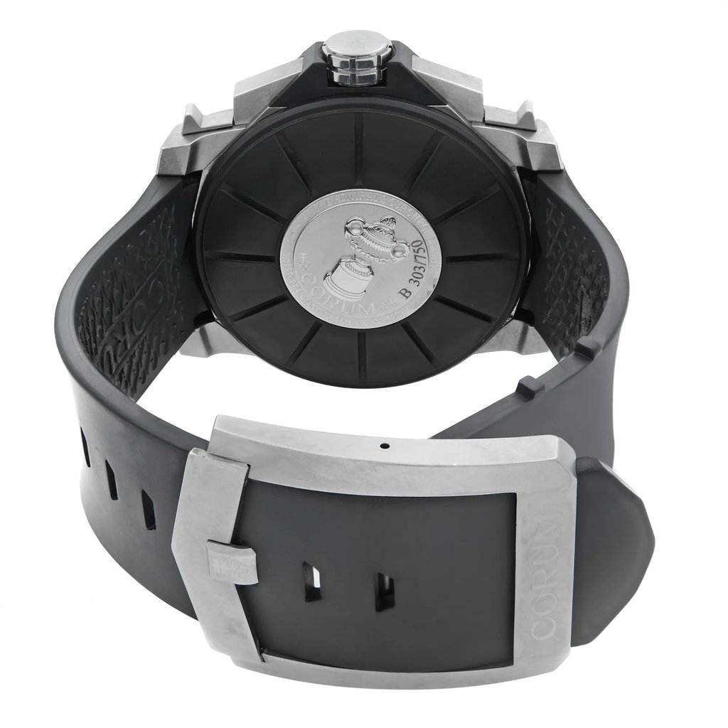 An image of a pre-owned wristwatch showing the back view, focusing on the closed clasp. The watch features a black rubber strap with a textured pattern on the inner side. The clasp is metallic and engraved with the brand name "CORUM." The watch's back case is prominently displayed, revealing an embossed design. The angle is slightly elevated, providing a clear view of the clasp and case, and the image is taken from a close distance.