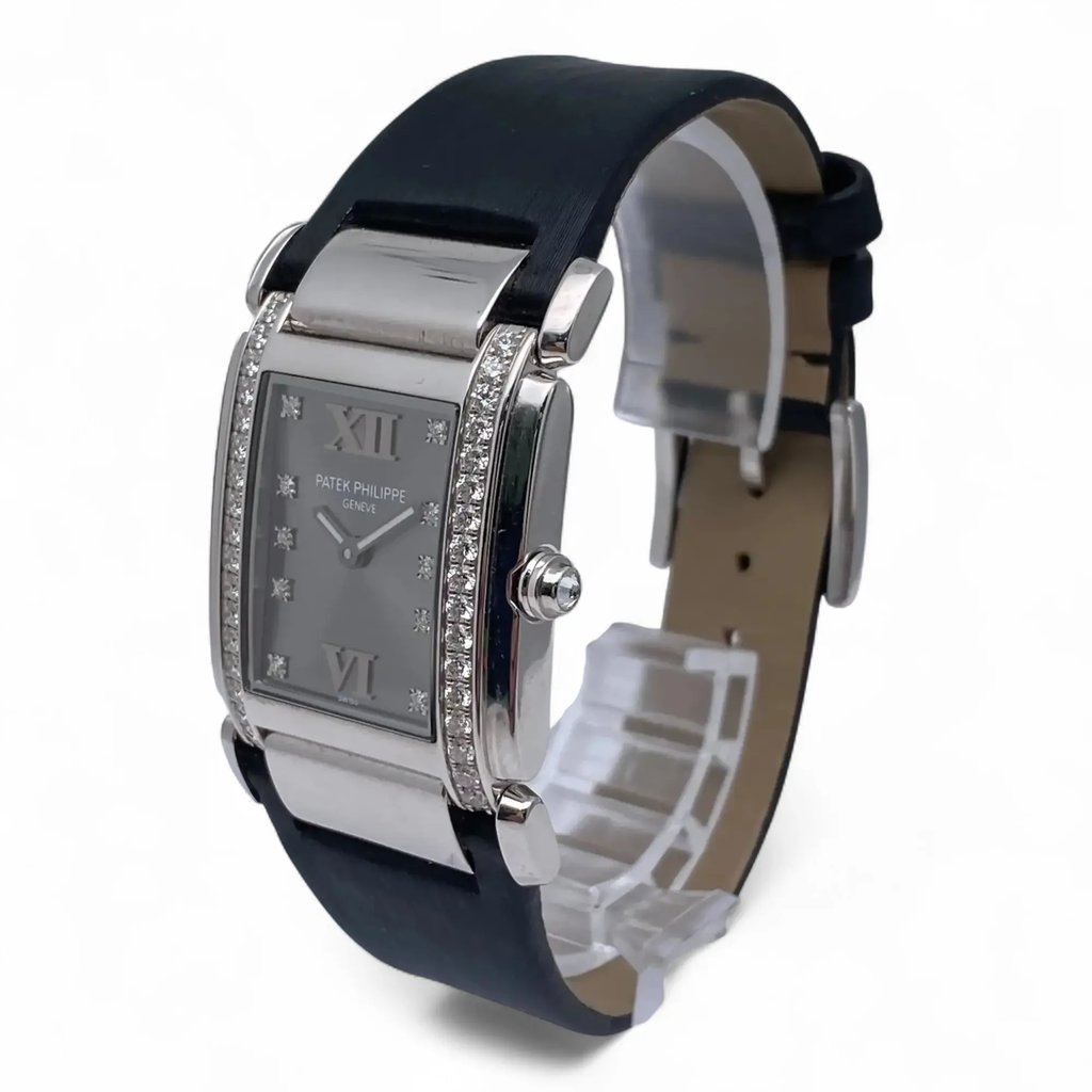 An image of a pre-owned women's Patek Philippe wristwatch, taken from a front-angle perspective. The watch features a rectangular face adorned with Roman numerals at the 12 and 6 positions, surrounded by two vertical rows of small diamonds. It has a black strap, and the watch is positioned at a slight angle to showcase its elegant design, with the crown visible on the right side. The photo is taken from a moderate distance, providing a clear view of the watch's details.