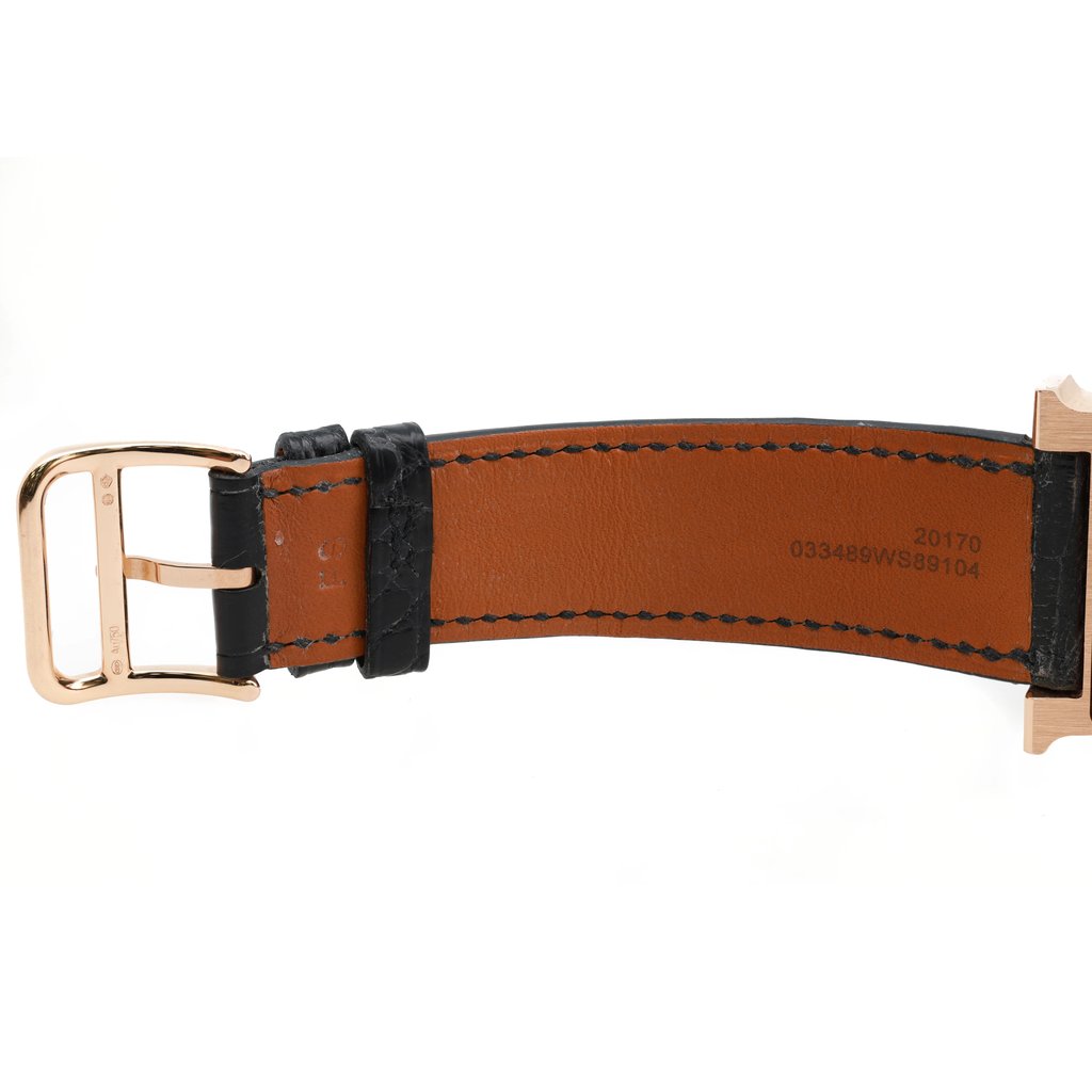 An image of a pre-owned Hermès women's wristwatch shown from a side angle. The focus is on the leather strap, which is brown with black edges and stitching. The gold-tone buckle is visible on the left side, and the strap is slightly curved. The image captures the watch at a close distance, highlighting the texture and details of the strap and buckle.