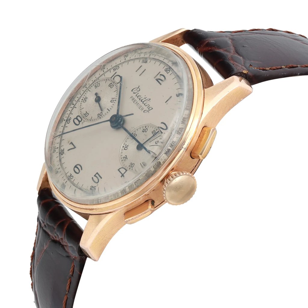 An image of a pre-owned Breitling men's wristwatch in a classic style, captured from a side profile angle that showcases the crown. The watch features a silver dial with patina, a rose gold bezel and case, and an aftermarket dark brown leather band with visible stitching. Visible scratches on the csytal due to aging. The dial includes a small seconds subdial and is positioned at a close distance, providing a clear view of the watch's details.