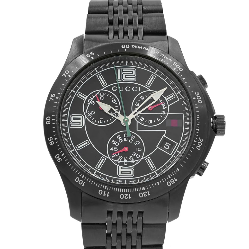 An image of a pre-owned Gucci men's wristwatch in a dress/formal style, displayed in a front close-up shot that centers on the watch face. The round watch face is black with a matching black bezel, complemented by a stainless steel band. It features 12-hour dial with Arabic numerals and stick indexes, a chronograph, luminous hands, and a small seconds subdial. The Gucci logo is prominently displayed at the 12 o'clock position, and the image is taken from a direct front angle, showing the watch in full detail at a close distance.