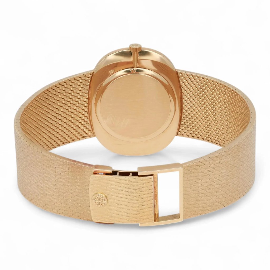 An image of a pre-owned Patek Philippe unisex wristwatch. The watch is positioned with its back facing the viewer, showcasing the closed clasp and textured yellow gold band. The angle is slightly above and from behind, providing a clear view of the back of the watch case and the intricate mesh pattern of the bracelet. The photograph is taken at a close distance, emphasizing the details of the watch's design.