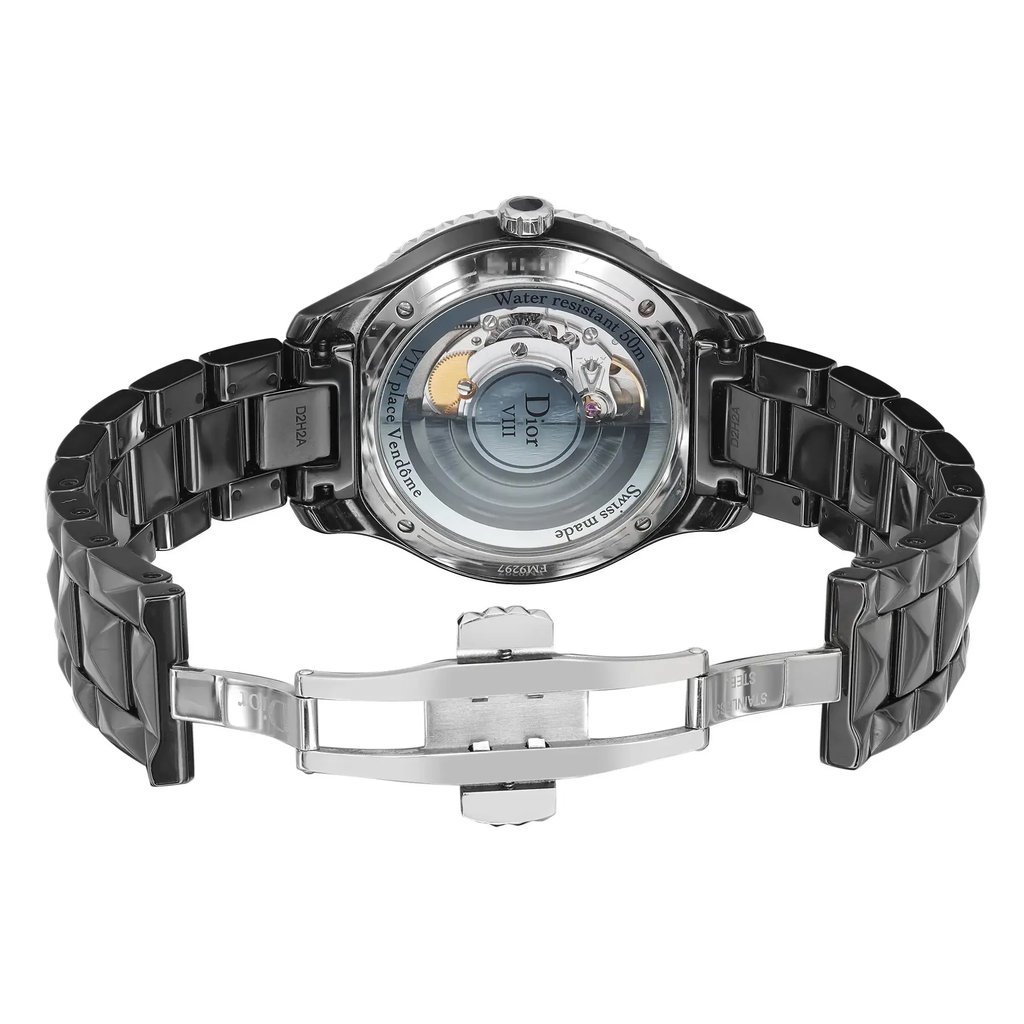 An image of a pre-owned wristwatch shown from the back view with the clasp open. The watch is positioned centrally, with a slight upward angle, allowing a clear view of the intricate inner workings through the transparent case back. The metal bracelet is visible, showcasing a polished finish. The image is taken from a moderate distance to capture the entire back of the watch and the open clasp.