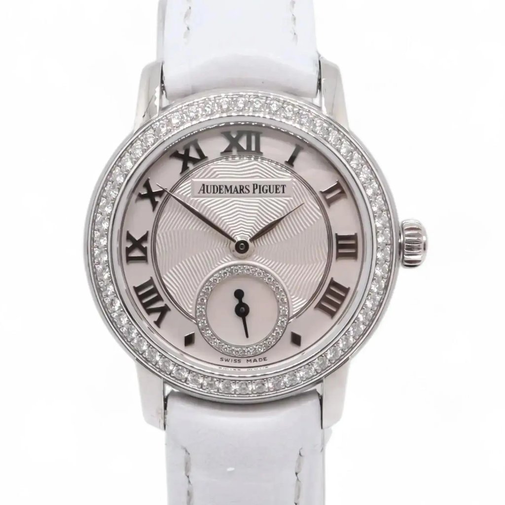 An image of a pre-owned women's Audemars Piguet wristwatch, taken from a front-facing angle at a close distance. The watch features a circular face with Roman numerals, a smaller subdial, and a diamond-encrusted bezel. The strap is white, and the brand name is visible on the dial.