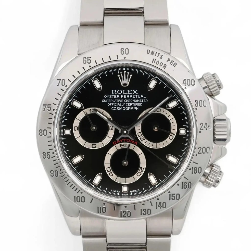 An image of a pre-owned men's Rolex wristwatch, captured from a straight-on angle, displaying the full face and part of the bracelet. The watch features a black dial with luminous hands, a chronograph, and three subdials, including a small seconds subdial. The silver bezel is engraved with a tachymetric scale. The watch is positioned centrally in the frame, filling most of the image space, providing a clear and detailed view.