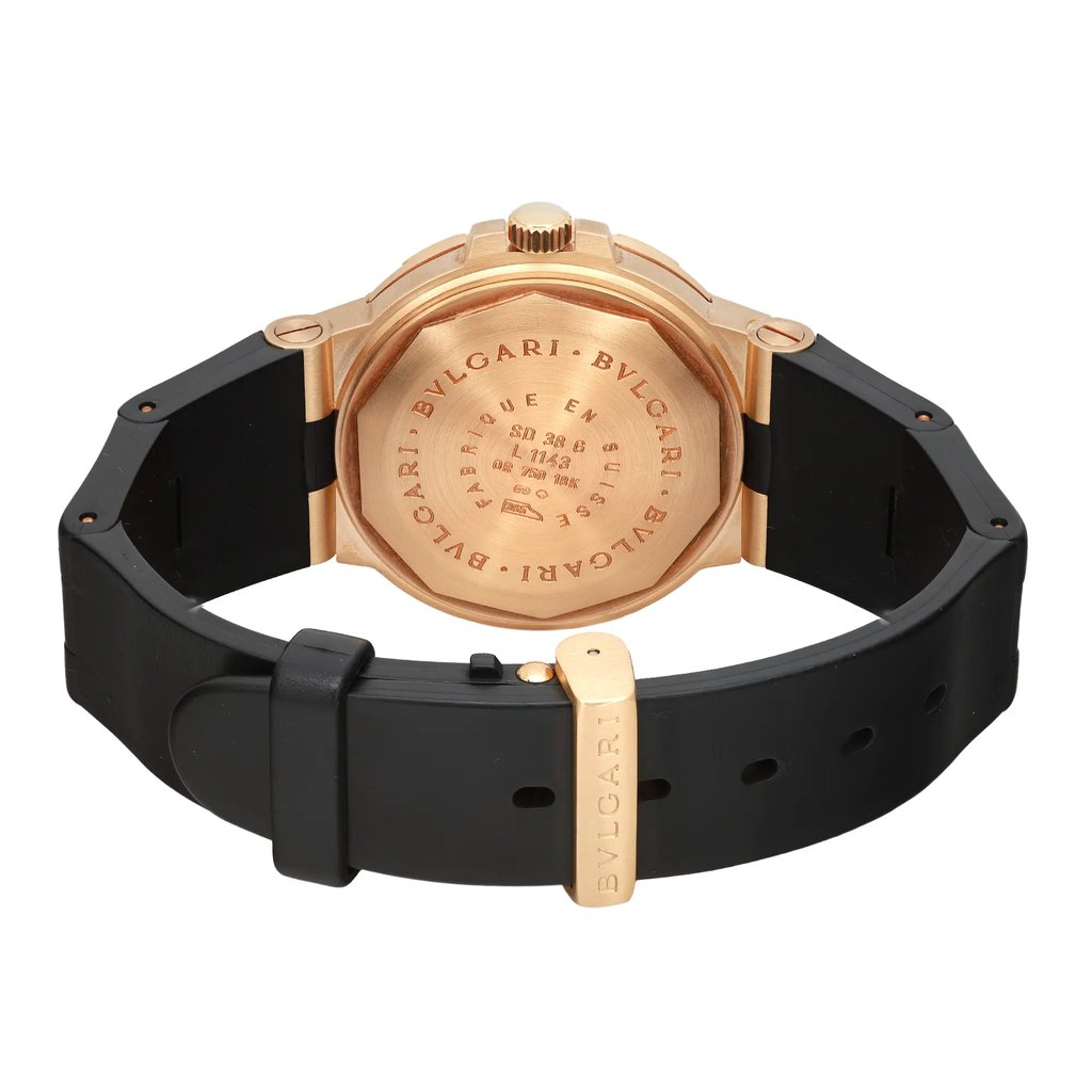 An image of a pre-owned Bvlgari men's wristwatch showcasing the back view. The watch has a round case made of yellow gold with a screwback featuring the brand's engravings. It is attached to a rubber black band and the yellow gold deployant clasp is visible and closed. The perspective is a close-up at a straight angle, emphasizing the details of the case back and clasp. The band shows minor signs of wear and light signs of scratches.