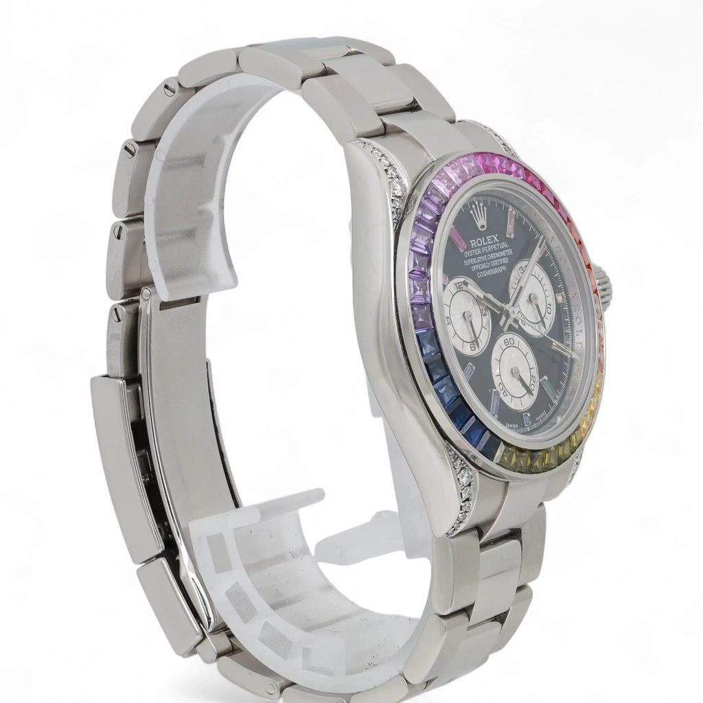 An image of a pre-owned men's Rolex wristwatch, positioned at a slight angle to the right. The watch features a metallic band and a chronograph with luminous hands. The face includes a small seconds subdial, and the bezel showcases a gradient of colorful stones. The image is taken from a close distance, highlighting the intricate details of the watch's design.
