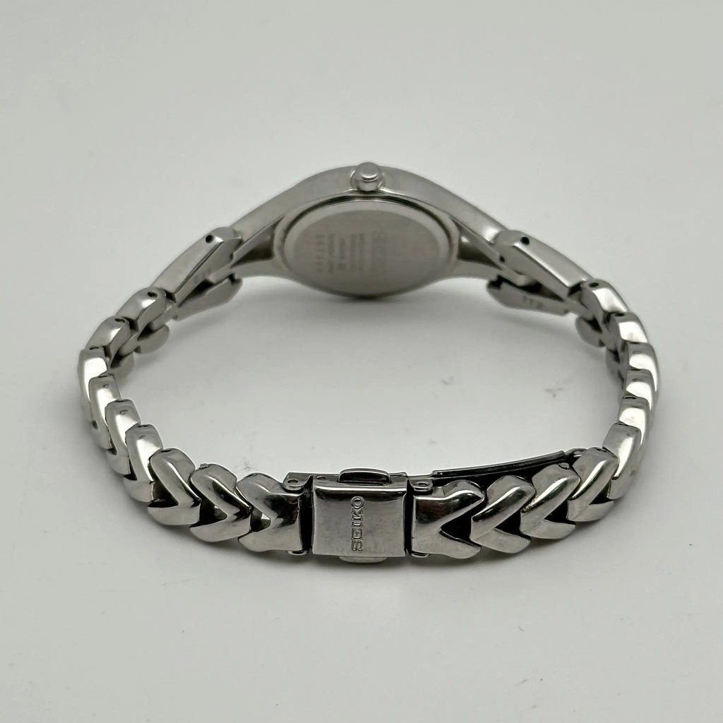 An image of a Wristwatch by Seiko. This Pre Owned item is designed for Women, featuring a Casual style. It has a Quartz movement and an Analog display with a White dial color. The indices include 12-Hour Dial,Diamond Markers. The band is made of Stainless Steel and the case is made of Stainless Steel. The watch has a Round shape with a case size of 22 mm and a case thickness of 7mm.