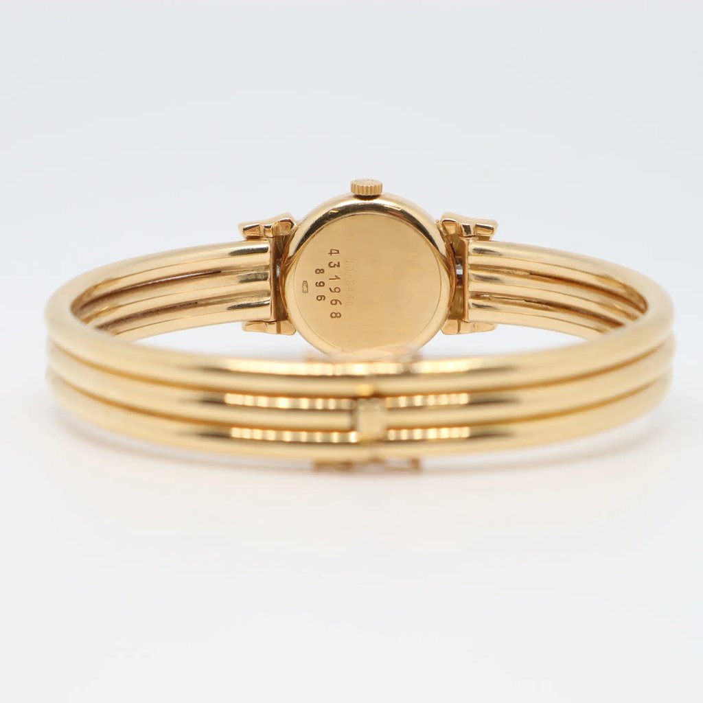 An image of a pre-owned women's wristwatch by Chopard. The watch is positioned upright, displaying its back case with engraved numbers. It features a yellow gold design with a triple-band bracelet. The angle is slightly elevated, capturing the watch from a close distance against a light background.