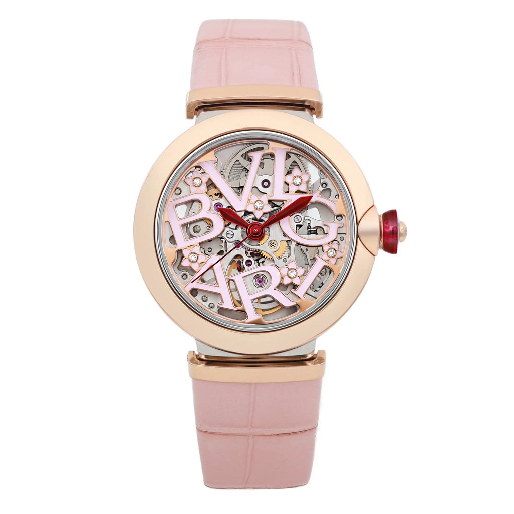 An image of a pre-owned wristwatch displayed from a front full frontal view. The watch features a pink strap with a rose gold bezel. The dial showcases intricate mechanical details and the brand name in stylized lettering. The crown is adorned with a decorative element, adding to the watch's elegant design.