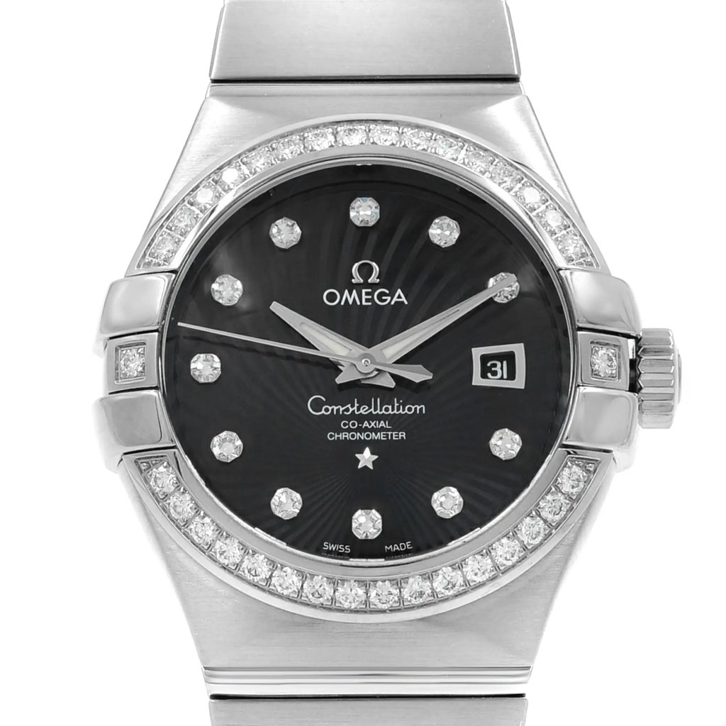 An image of a luxury OMEGA women's wristwatch, shown in a front close-up shot emphasizing the watch face. The round dial is black with the OMEGA logo and 'Constellation co-axial chronometer' text, and features diamond indices and luminous hands. A date indicator is present at the 3 o'clock position. The bezel is adorned with a ring of diamonds. Both the band and case are made of white gold, and the condition of the display model is excellent. The watch is captured from a direct front angle and at a close distance, providing a clear view of its elegant details.