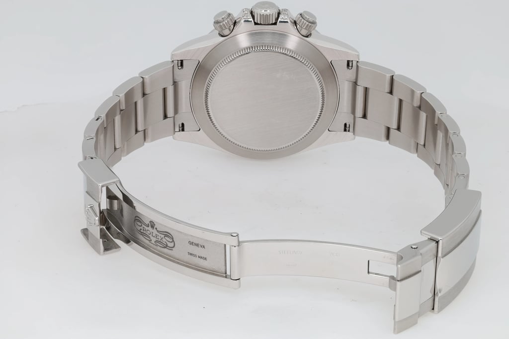 An image of a pre-owned men's Rolex wristwatch, viewed from the back at a slight angle, showcasing the closed clasp and bracelet links. The watch is positioned centrally, with the focus on the detailed engravings on the clasp. The angle highlights the chronograph buttons and the polished finish of the watch, emphasizing its craftsmanship and design features.