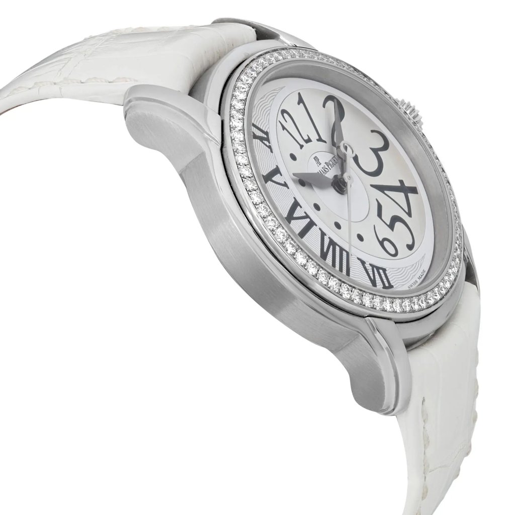 An image of a pre-owned Audemars Piguet women's wristwatch, viewed from a three-quarter angle. The watch is positioned to the left, showcasing its white leather strap and silver-toned case adorned with a diamond bezel. The face of the watch features bold black numerals on a reflective silver dial. The angle highlights the watch's elegant design and intricate detailing.