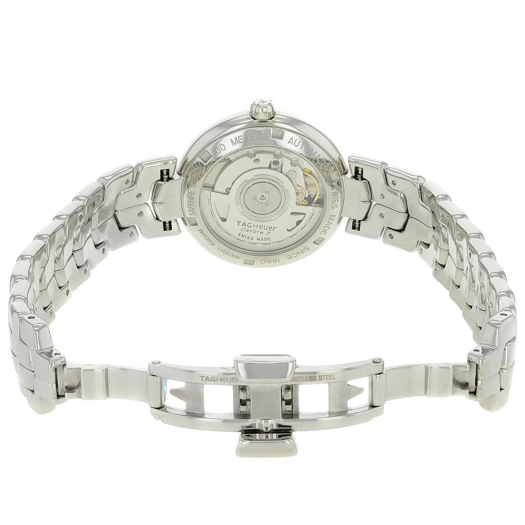 An image of a pre-owned TAG Heuer women's wristwatch, showcasing the back view with an open clasp. The stainless steel case features an exhibition caseback, revealing the watch's inner mechanics. The round watch shape complements the matching stainless steel band. The double-locking fold-over clasp is prominently displayed in the foreground, with the watch positioned at a slightly elevated angle, capturing the details of the clasp and band from a close distance.