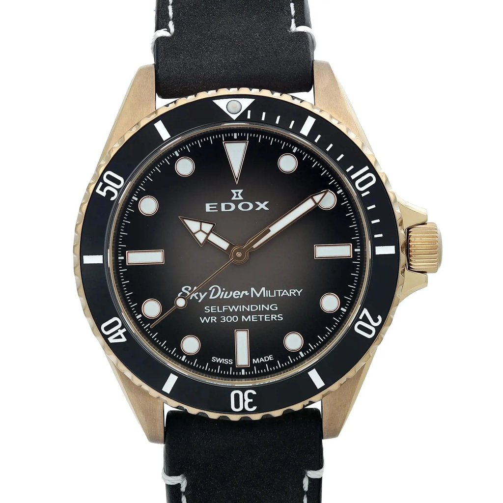 An image of a pre-owned wristwatch taken from a front close-up angle. The watch features a black face with white hour markers and hands. The bezel is marked with minute indicators, and the crown is positioned on the right side. The brand name and model details are visible on the watch face. The strap is black with white stitching.