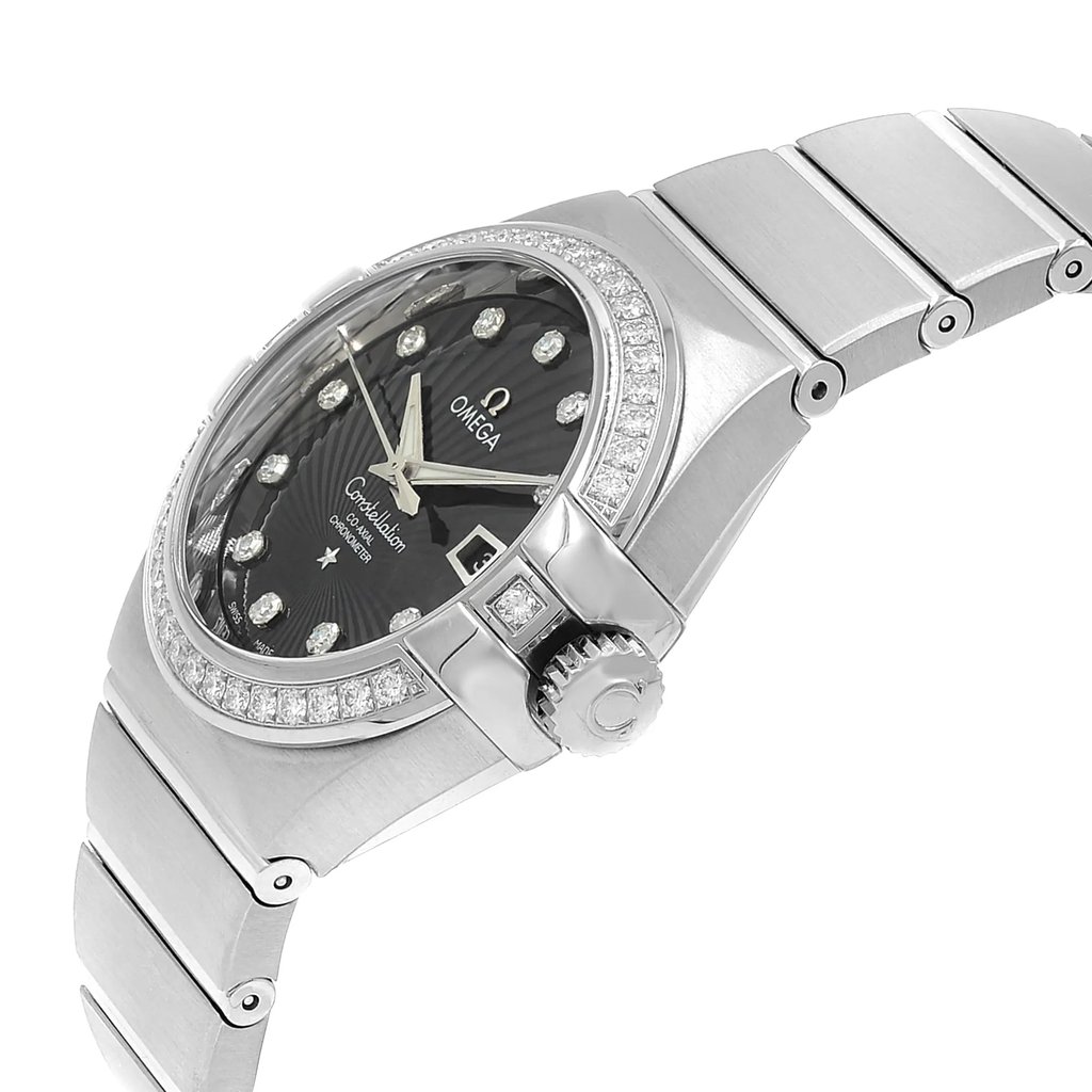 An image of a luxury OMEGA women's wristwatch, shown in a display model condition with a side profile view that emphasizes the crown. The watch features a round white gold case with a black dial, luminous hands, and a date indicator, surrounded by a diamond-studded bezel. It has a white gold band, and the image is taken at a close distance, capturing the fine details and angles of the watch's design.
