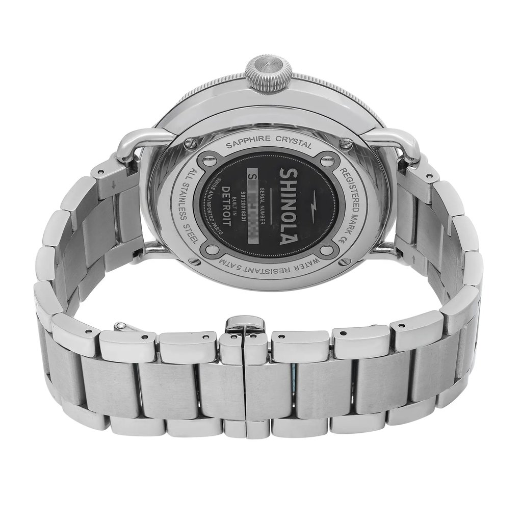 An image of a wristwatch viewed from the back, showcasing the clasp and stainless steel bracelet. The watch, positioned in the center, features a circular case with visible screws and brand markings. The angle is slightly elevated, focusing on the closed clasp. The photograph is taken from a close distance, highlighting the watch's polished metal finish and intricate details.