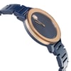 An image of a wristwatch taken from a side profile view opposite the crown, showcasing the sleek design. The watch features a smooth, round face with a gold-toned bezel and deep blue dial. The bracelet is a matching blue with a glossy finish. The angle highlights the watch's elegant curves and the seamless integration of the band with the case. The photograph is taken at a close distance, emphasizing the details of the watch's construction and finish.