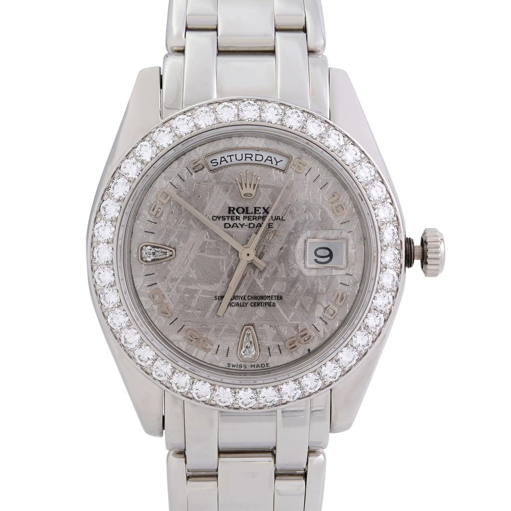 An image of a pre-owned wristwatch showing a close-up, front view of the watch face. The watch features a circular bezel adorned with diamonds, a textured dial displaying the day at the top and the date at the three o'clock position. The hands and hour markers are elegantly designed, and the watch has a polished metal band. The image focuses on the details and craftsmanship of the watch, highlighting its luxurious design.