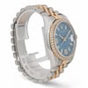 An image of a pre-owned unisex adult Rolex wristwatch with a date indicator feature. The watch is positioned at a slight angle, showcasing the side and partial front of the timepiece. The blue dial is visible, encased in a diamond-studded bezel, and the watch's two-tone metal band is prominently displayed. The photograph is taken from a close distance, emphasizing the intricate details of the watch's design.
