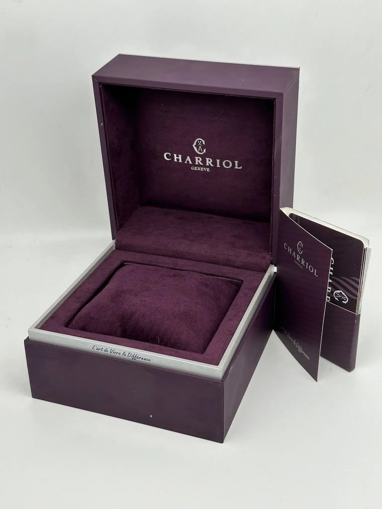 An image of a wristwatch box from Charriol, viewed from a slightly elevated angle. The box is open, showcasing its plush, dark purple interior with the brand name "CHARRIOL" and "GENEVE" printed on the inside back. In front of the box, there is a matching booklet partially visible. The box is positioned centrally, and the photo captures it up close, filling most of the frame.