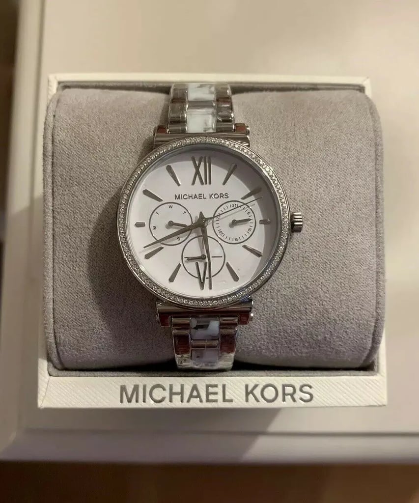 An image of a Wristwatch by Michael Kors. This Display Model item is designed for Women, featuring a Dress/Formal style. It has a Quartz movement and an Analog display with a White dial color. The indices include Roman Numerals. The band is made of Ceramic,Stainless Steel and the case is made of Stainless Steel. The watch has a Round shape with a case size of 36 mm and a case thickness of 9 mm.