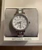An image of a Wristwatch by Michael Kors. This Display Model item is designed for Women, featuring a Dress/Formal style. It has a Quartz movement and an Analog display with a White dial color. The indices include Roman Numerals. The band is made of Ceramic,Stainless Steel and the case is made of Stainless Steel. The watch has a Round shape with a case size of 36 mm and a case thickness of 9 mm.