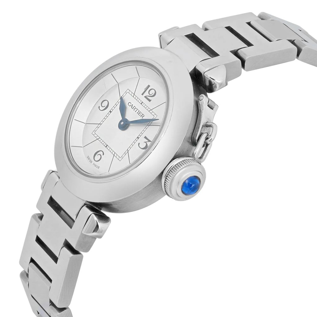 An image of a pre-owned women's Cartier wristwatch. The watch is positioned at a slight angle, showcasing the round silver dial with black numerals and blue hands. The stainless steel bracelet is partially visible, and the crown features a blue cabochon. The photograph is taken from a close-up perspective, highlighting the watch's elegant details.