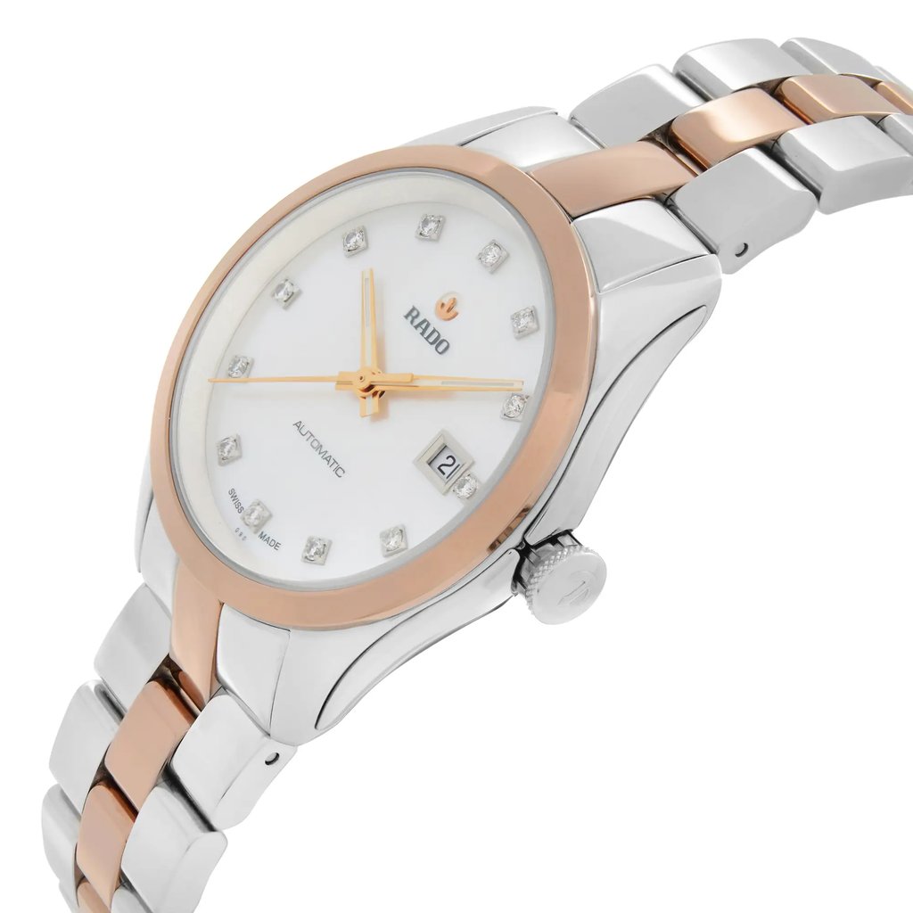 An image of a wristwatch in a side profile view, showcasing the crown. The watch has a two-tone metal band with a silver and rose gold finish. The face is white with diamond hour markers and gold-tone hands. The date is displayed at the 3 o'clock position. The image captures the watch at a close angle, highlighting its elegant design and details.