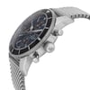 An image of a pre-owned Breitling men's wristwatch with a casual style, captured from a side profile angle showing the crown. The watch features a round stainless steel case and band, with a sunburst blue dial and black bezel. It includes a chronograph, date indicator, luminous hands, and a small seconds subdial. Visible scratches can be seen on the bezel insert, and minor nicks are present on the case and case back. The photograph is taken at a close distance, emphasizing the watch's details and signs of wear.