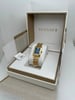 An image of a Versace women's wristwatch displayed at a slight angle, positioned centrally within an open box. The watch features a rectangular gold case and bracelet with a blue dial. The image is taken from a close distance, showcasing the elegant design and intricate details. The box is lined with white and gold, with the brand name prominently visible on the inside lid.