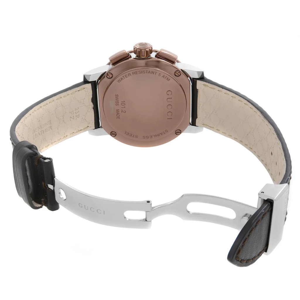 An image of a new men's Gucci wristwatch with defects, viewed from the back with an open deployant clasp. The watch features a round stainless steel case with a screwback, displayed at a straight angle and close distance. It has a leather band with visible texture and the Gucci logo on the metal parts of the clasp.