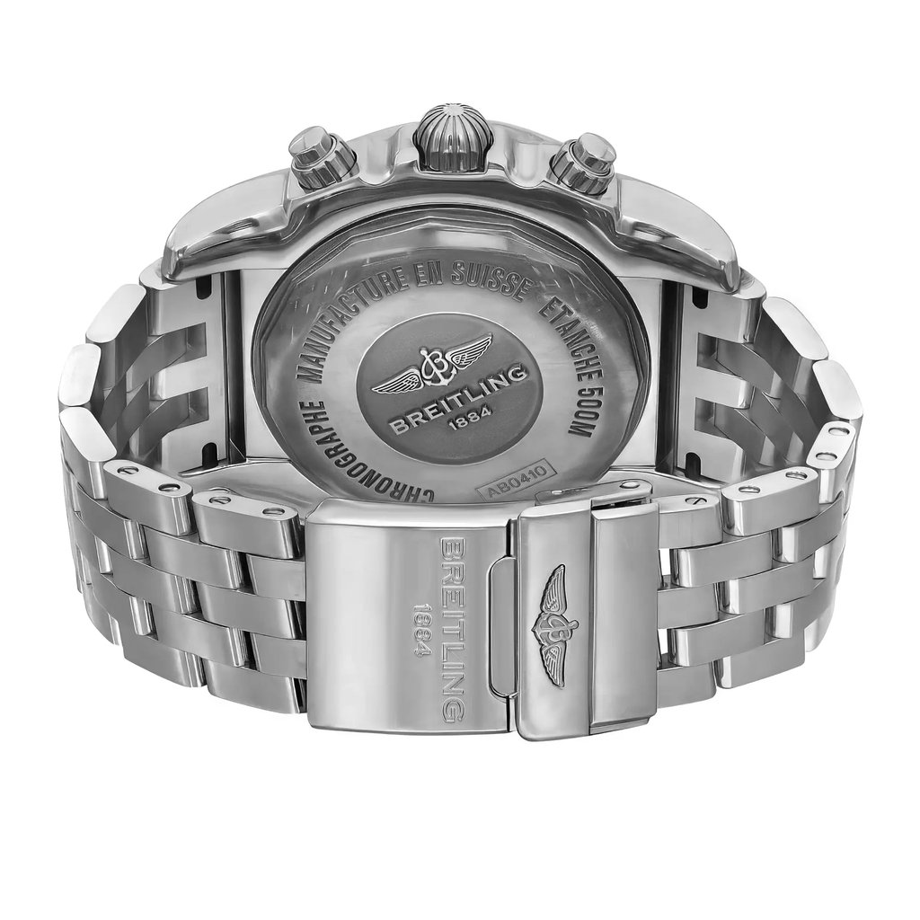 An image of a pre-owned Breitling men's wristwatch positioned to show the back view. The stainless steel caseback with a screwback design is centered and in focus, featuring the Breitling logo and inscriptions. The round watch is attached to a stainless steel band, and the fold-over clasp with flip lock safety is partially open, angled to the right of the frame. The band segments are visible on either side of the clasp, indicating the watch's substantial size. The watch features include a date indicator, GMT, luminous hands, and a small seconds subdial, but these are not visible from this angle. The image is taken from a close distance, capturing fine details and textures of the metal surfaces.