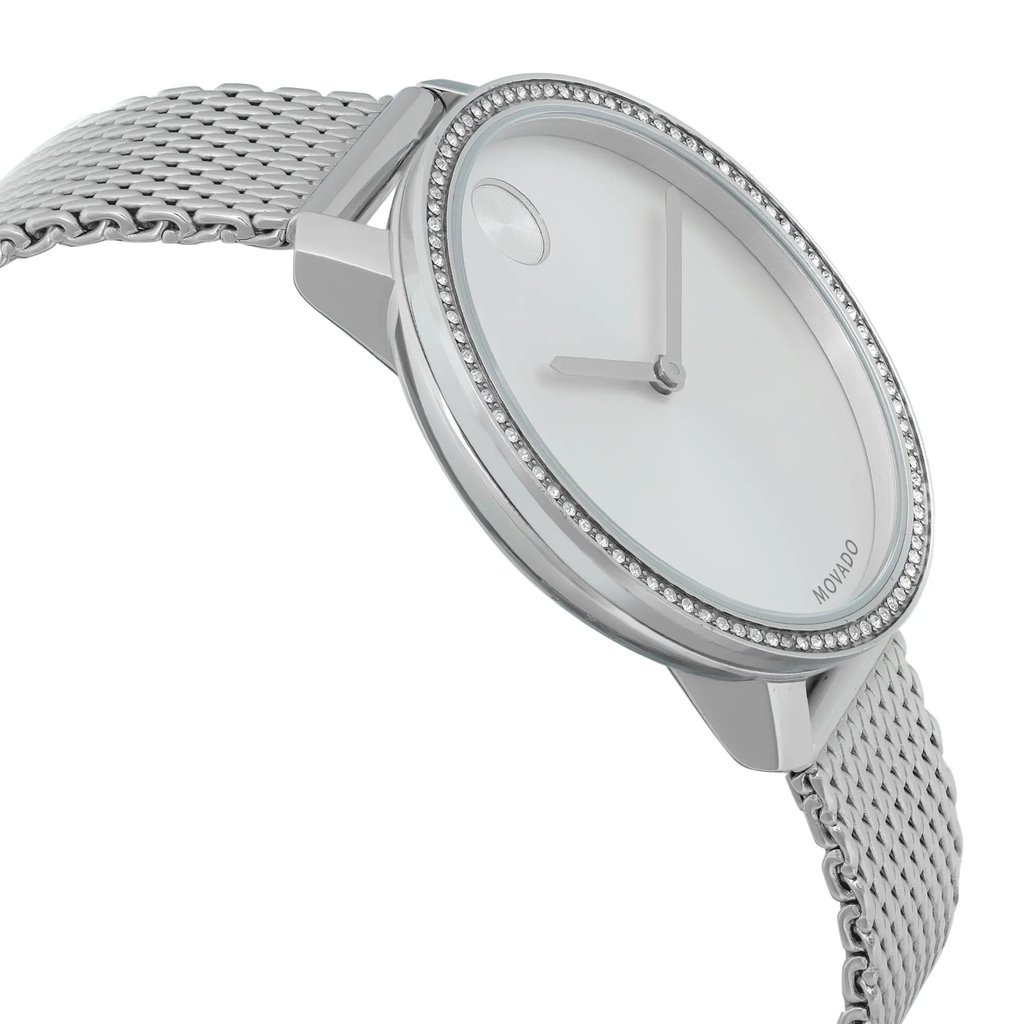 An image of a pre-owned wristwatch viewed from the side profile, opposite the crown. The watch features a minimalist design with a silver mesh band and a round case adorned with a bezel of small crystals. The face is simple, with two slender hands and a single dot at the 12 o'clock position. The angle highlights the sleek profile and elegant detailing of the watch, captured at a close distance.